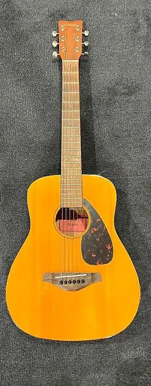A yellow acoustic guitar is sitting on a carpet.