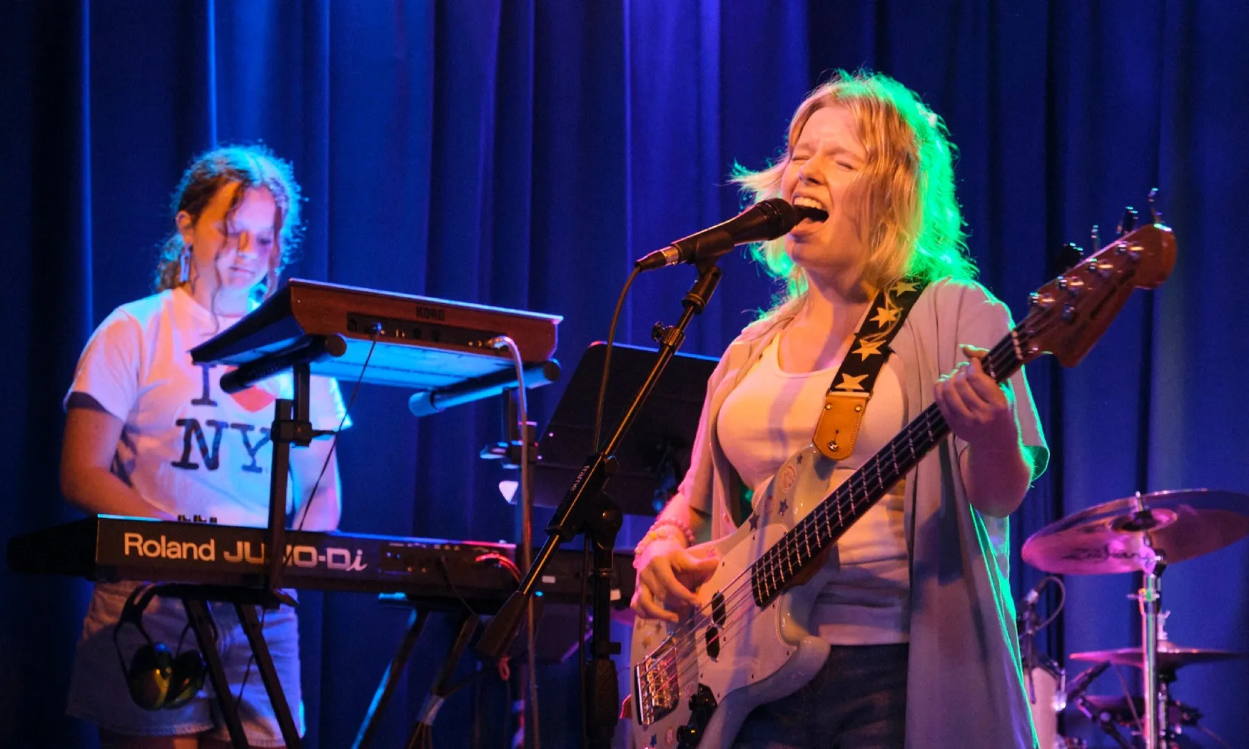 Two Sunburst students perform on stage, one singing and playing bass, one on keyboards