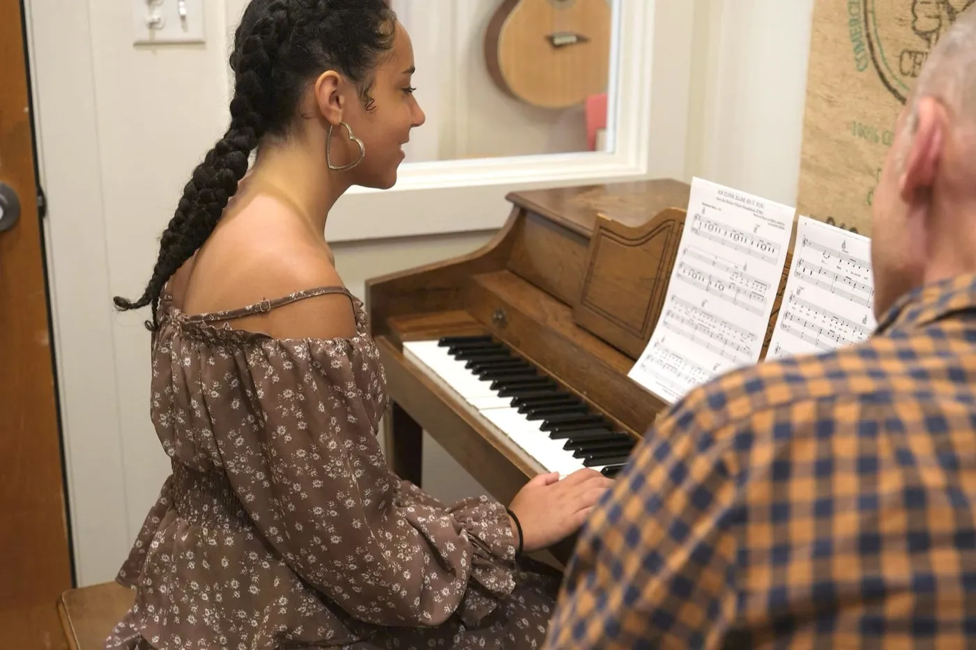 A student plays piano with sheet music while her teacher looks on