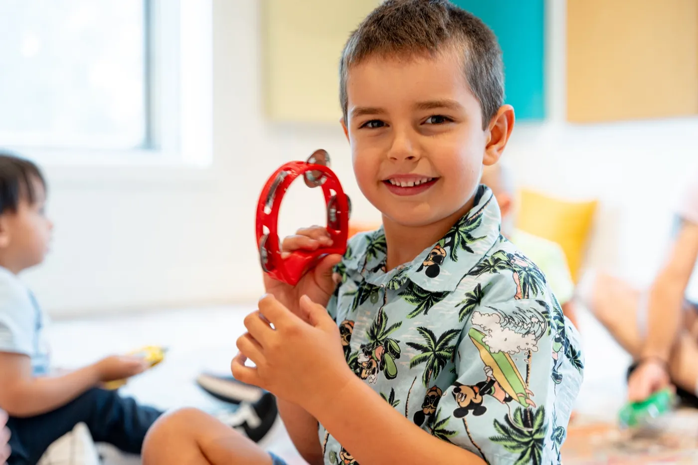 A smiling young child plays a red tambourine in a Music Together class