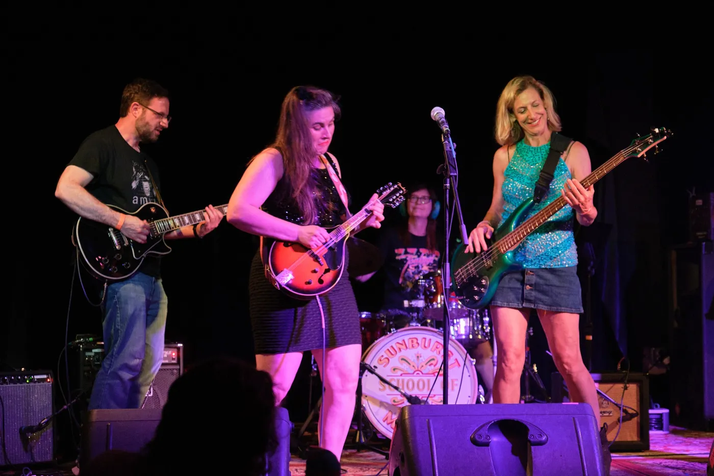 A Sunburst adult band performs on stage with the Sunburst School of Music drum head
