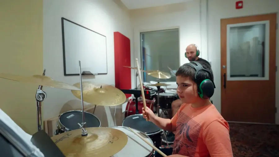 A young drummer in headphones plays a full kit in a soundproof drum room