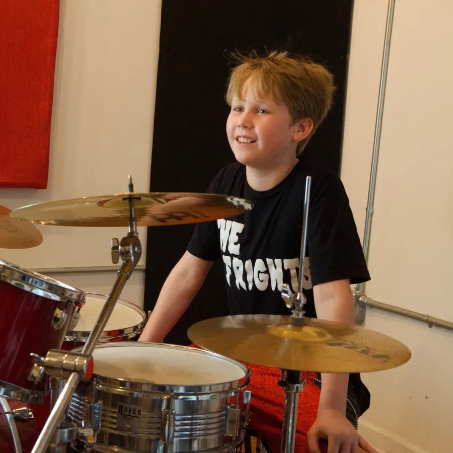 A young drummer grins mid-song behind the kit in a lesson room